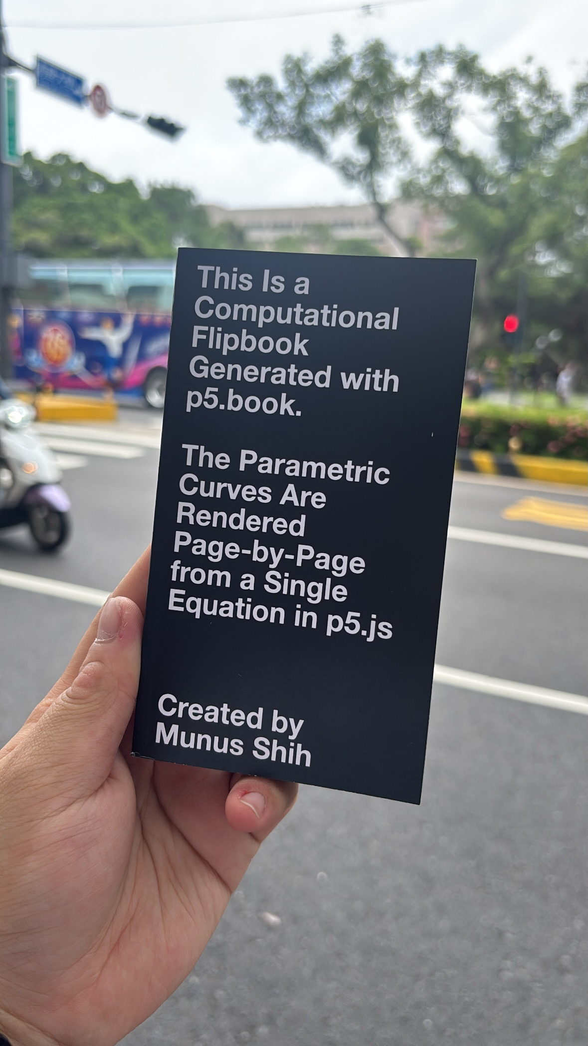 A hand holding a tall black computational flipbook outdoors